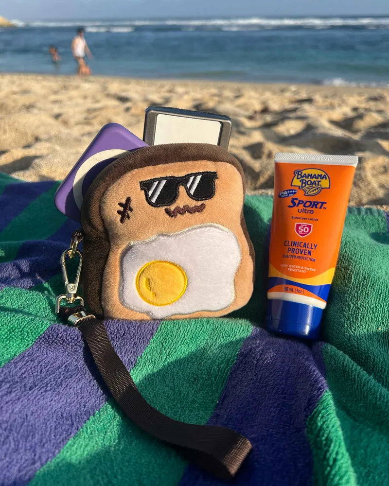 Burnt Toasty pouch on a striped beach towel, with sand and the sea behind it.